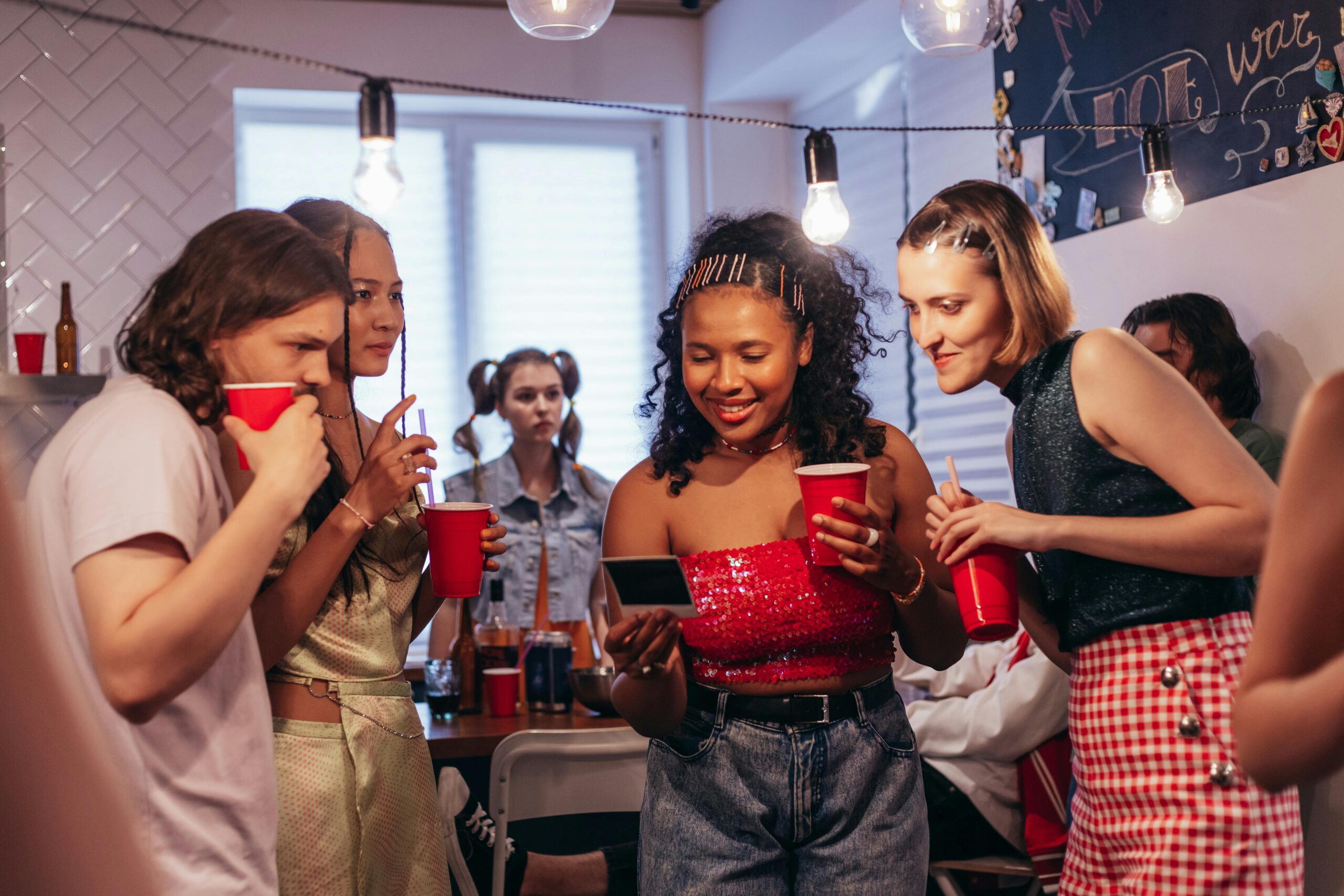 Group of young adults enjoying a lively house party with red cups and Polaroid photos.